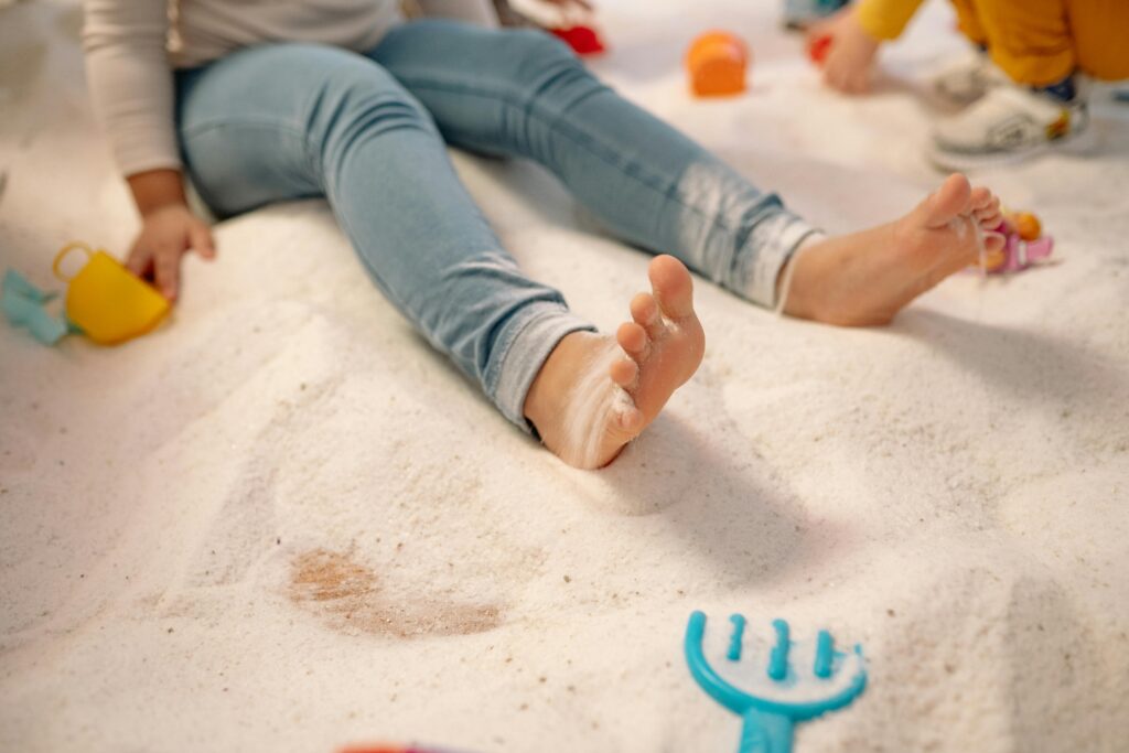 A child sitting in sand with toys, enjoying a playful indoor activity.