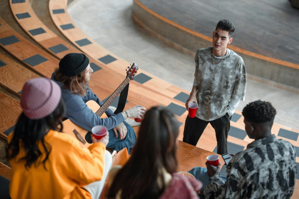 Friends enjoy a casual meetup with drinks and music at an amphitheater. High angle view enhances the connection.